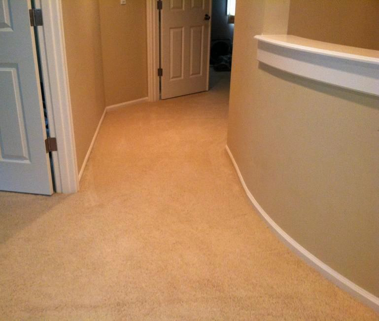 A carpeted hallway with beige walls and an open door at the end. A small ledge juts out from the right wall near the door.