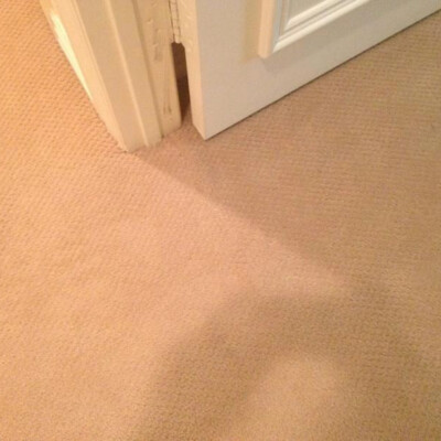 A beige carpeted floor with a white door slightly ajar, showing a small gap between the door and the floor.