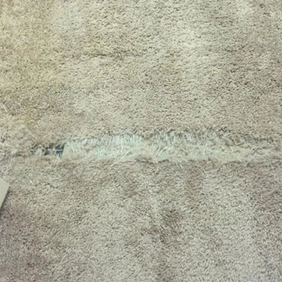 A beige carpet with a frayed and worn-out section along the seam between two rooms.