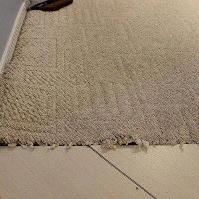 A close-up of a beige carpet fraying at the edge where it meets a tiled floor.