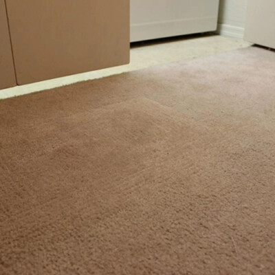 A close-up of a beige carpet with a visible rectangular indent, situated near a white wall, cabinets, and a door.