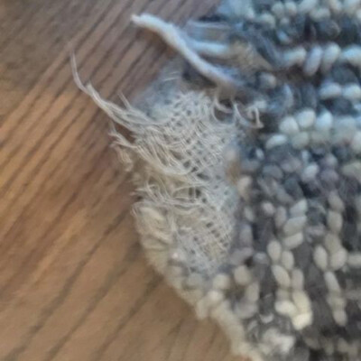 Close-up of a torn and frayed edge of a patterned rug on a wooden floor.