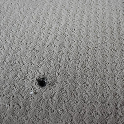 A light gray fabric with a small burned hole near the center.