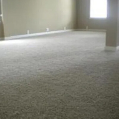 A large, empty room with beige carpet, beige walls, multiple windows, and a structural column near the center.