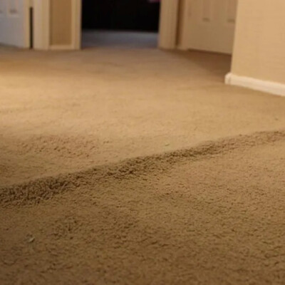 A beige carpet with a visible bump or ridge runs through a hallway with white doors and baseboards.
