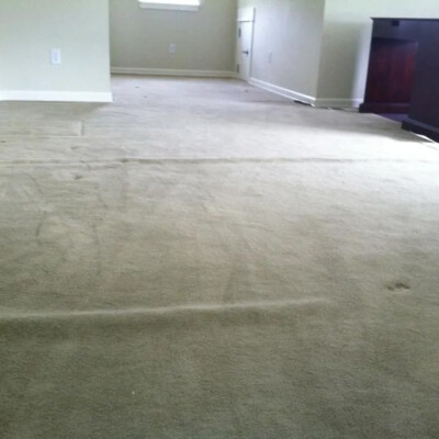 A partially empty room features a beige carpet and light-colored walls. A piece of dark wooden furniture is visible on the right.