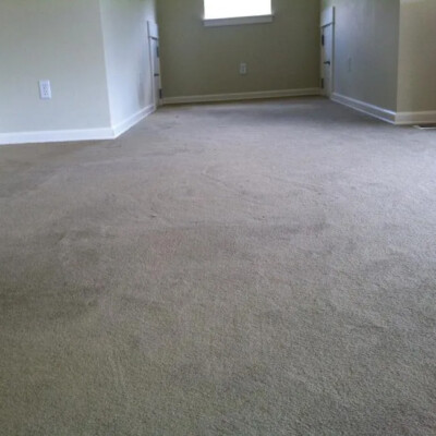 A room with beige carpet, light-colored walls, a small central window, and electrical outlets on the left wall.