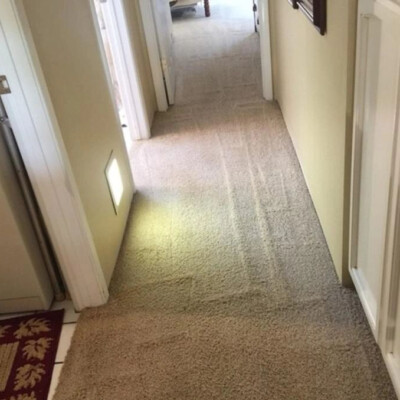 A carpeted hallway with light-colored walls, cabinets on the right, a washing machine on the left, and a small area rug near the washing machine. A dim light illuminates part of the hallway.