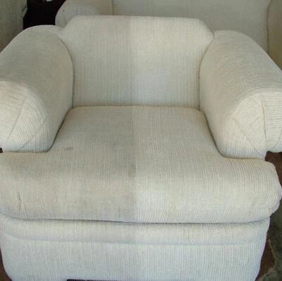 A beige armchair with rounded, cushioned armrests and a textured fabric finish, positioned on a carpeted floor.