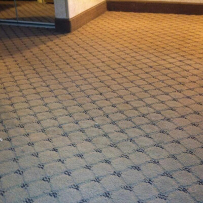 A carpeted floor with a brown geometric pattern next to a mirrored closet door in a room.