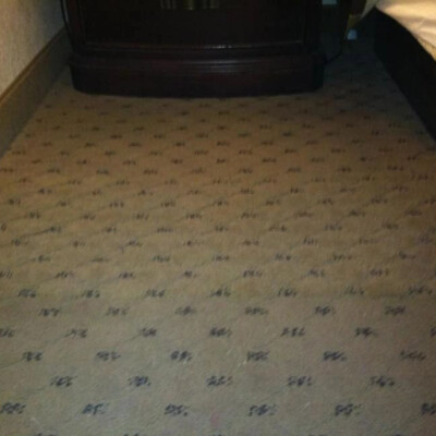 A patterned carpeted floor with a television stand partially visible in the background and a bed on the right side.