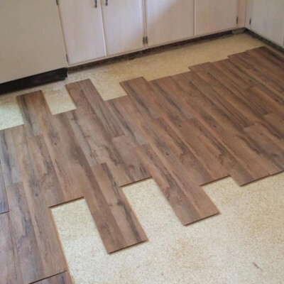 Partially installed wooden flooring with several planks laid out in a staggered pattern on top of an old linoleum surface in a kitchen space.